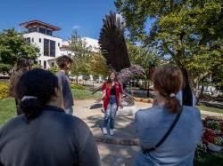 Female student ambassador conducting a tour and standing in front of the Red Hawk Statue on campus